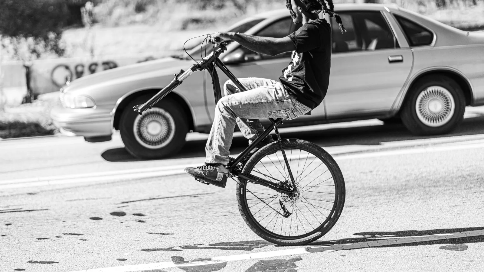 Young black man rides his bike alongside a 1990s car