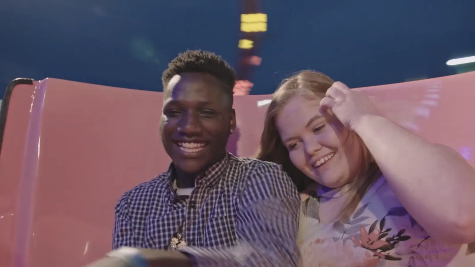 Two teens sit in a pink carnival ride.