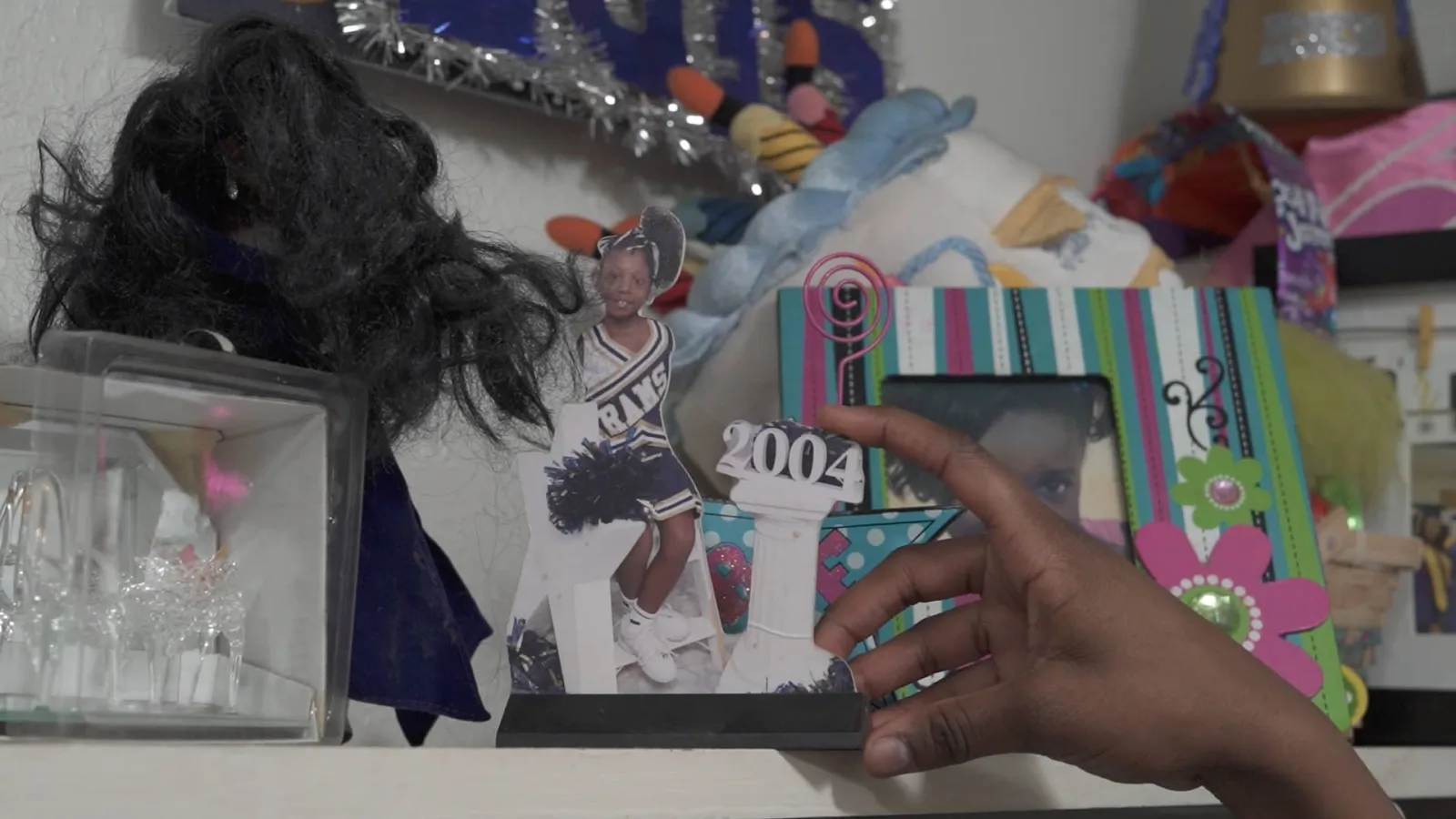 A dark-skinned hand points to a collage of imagery on a white wall shelf showcasing young girl's hobbies.